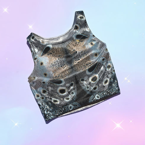A women's sleeveless racerback crop top with a body-hugging fit. The top features a detailed, kaleidoscopic all-over print inspired by deer pelt. The symmetrical, Rorschach-like design includes abstract spots and textures in shades of brown, blue, black, and grey, creating an intricate pattern that resembles a deer pelt.